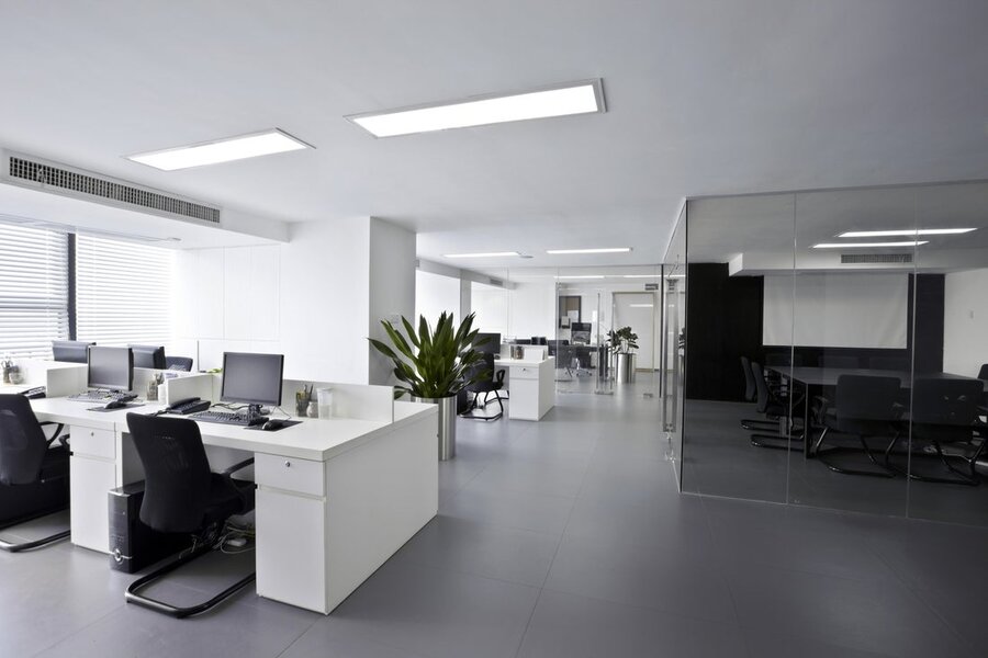 An office space with desks to the left and a conference room with glass walls to the right.