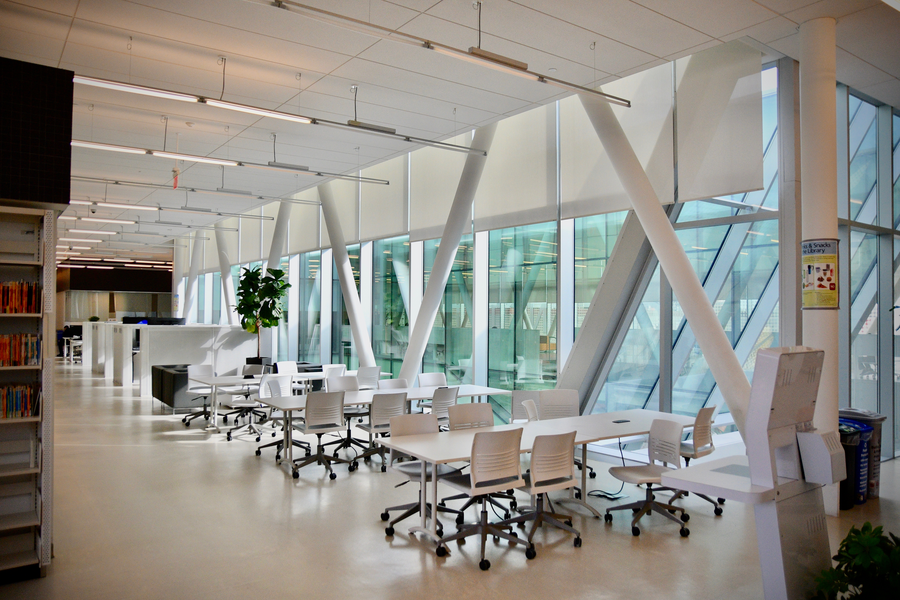 This is a modern office building's open work area with large windows featuring automated motorized shades that control natural light.