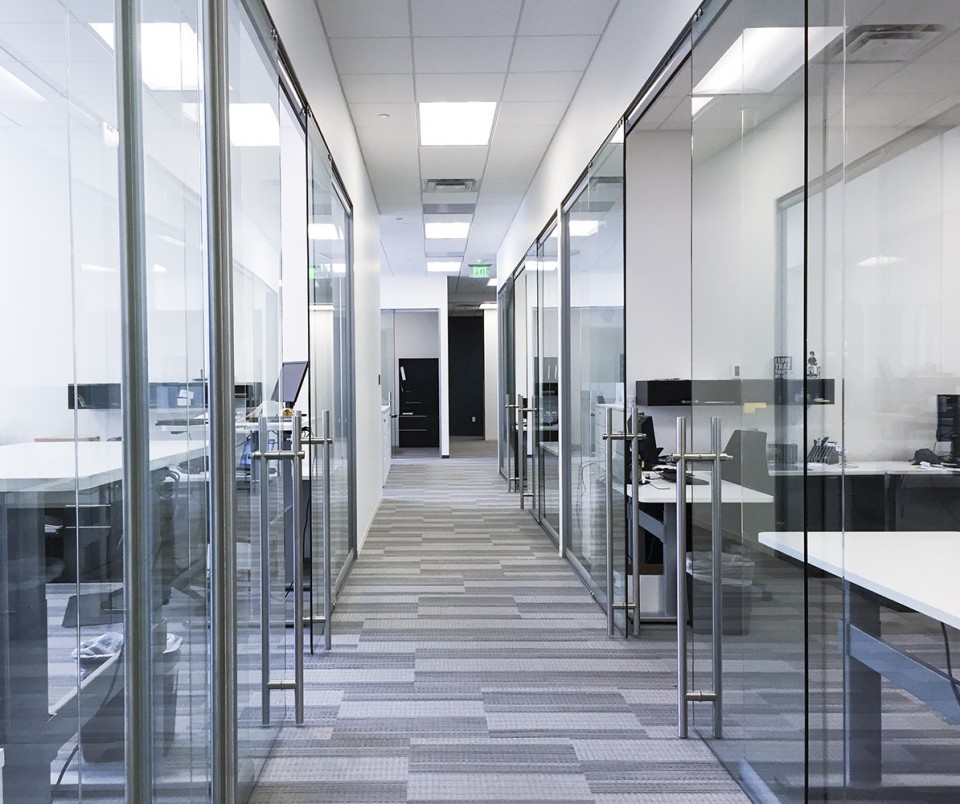 Modern office hallway with glass-walled workspaces and bright overhead lighting creating a clean, professional look.