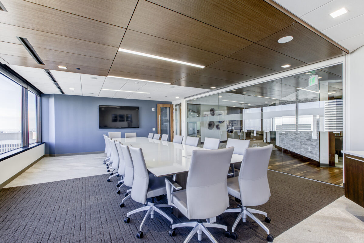 Modern conference room with a large wall display, glass walls, long white table, and ergonomic chairs in a professional office.
